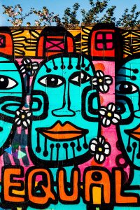 Brightly coloured urban graffiti mural artwork on wall with equal text and tribal faces