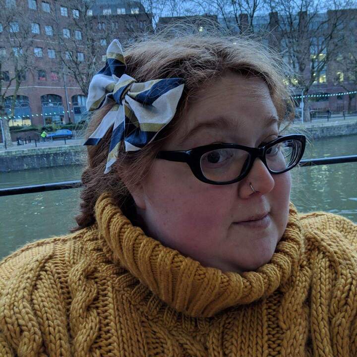 Talia by Bristol docks in a yellow jumper and black-framed glasses.