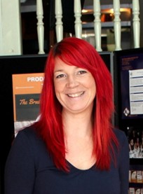 Susie Fisher, Director of A2i, smiling in front of a A2i exhibition stall. 