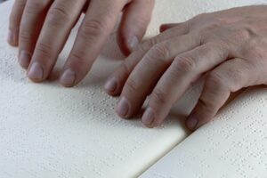 Hands gently resting on and reading raised Braille dots on an open book.