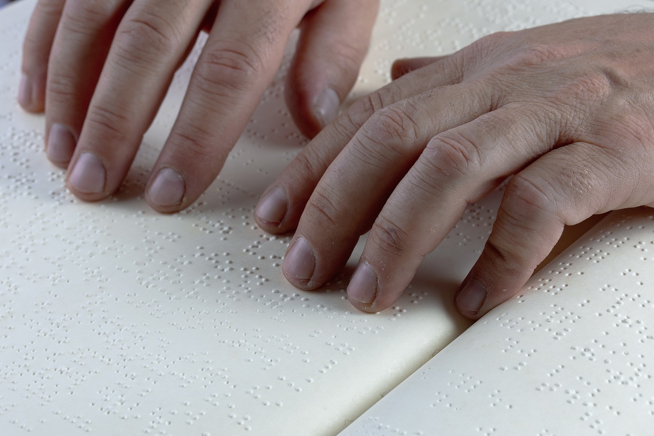 Hands gently resting on and reading raised Braille dots on an open book.
