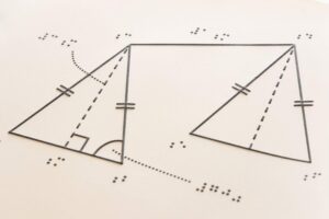 Tactile diagram of two geometric shapes drawn on white paper, showing triangles and quadrilaterals with marked equal sides, angles, and dashed construction lines.