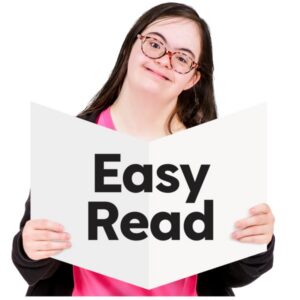 An individual holding a large white booklet open. The front cover of the booklet has bold black text reading “Easy Read.” The person is shown from the upper body, wearing a dark outer layer over a bright top.