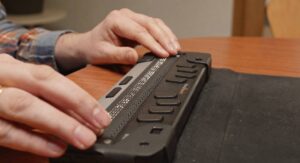 A person using a refreshable Braille display to access digital information through tactile Braille, demonstrating assistive technology for blind and visually impaired users.